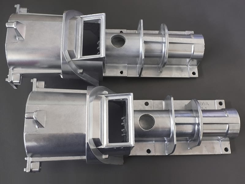The image shows a pair of metal parts on a gray surface, which appear to be part of a high-quality aluminum die casting machine. The metal parts are silver in color and have a glossy finish.