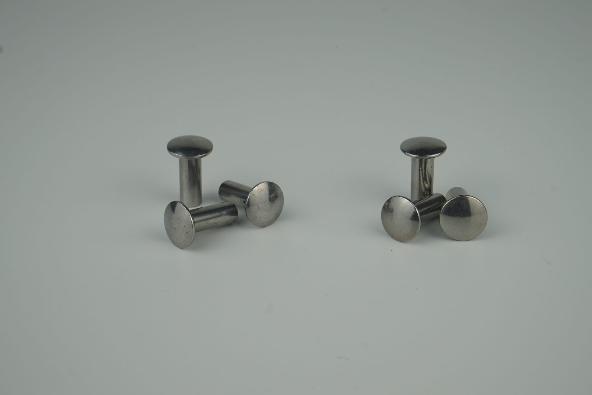The image shows a pair of stainless steel stud earrings on a white surface. The earrings have a sleek, metallic finish and are arranged in a symmetrical pattern. The background is a bright white, high