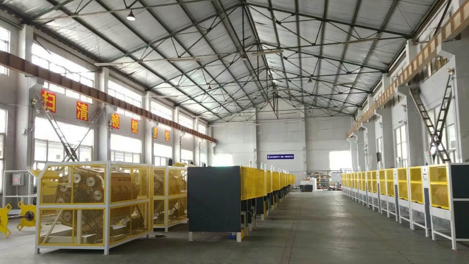 The image shows a large warehouse filled with lots of yellow and white machines on the floor, ladders on the right side, windows on the left side, and lights at the top. It appears to be a factory set