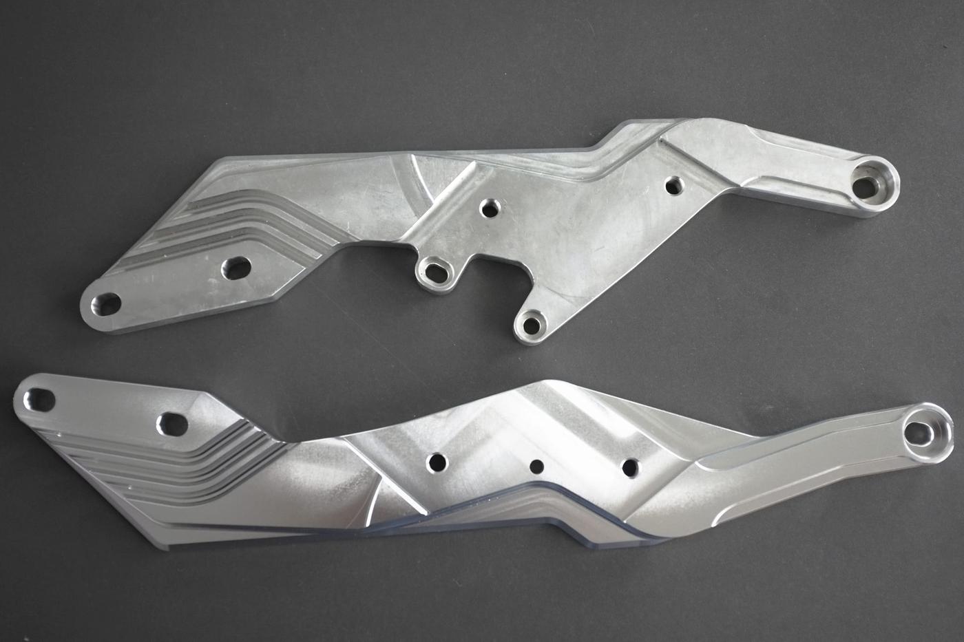 Aluminum motorcycle bracket parts before and after vibratory mass finishing showing matte cast surface versus bright satin finish